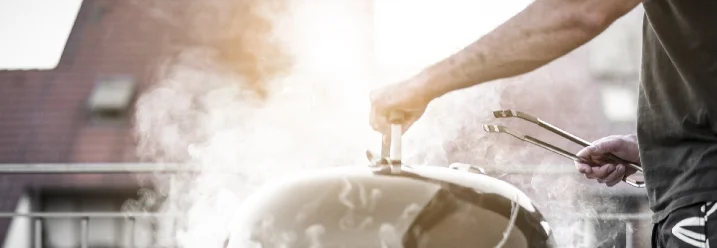 Person grillt mit Grillzange auf Balkon